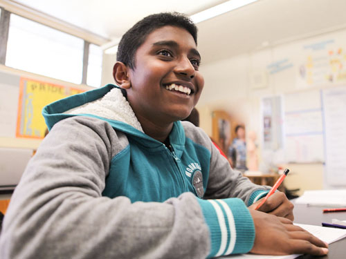 Image of a young male student smiling in class.