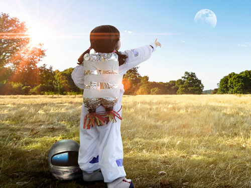 Young girl in an astronaut suit pointing at the moon.