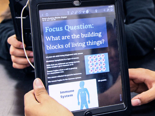 Student holding an iPad with a lesson on it called 