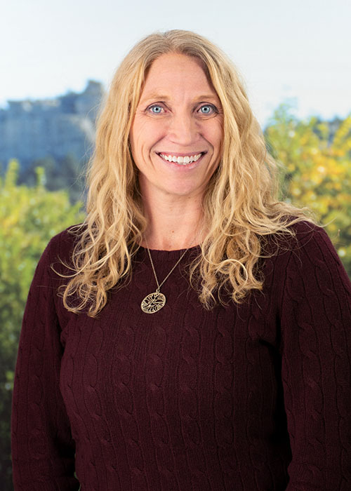 Holly Hereau is standing outside in Colorado Springs, Colorado in front of trees.