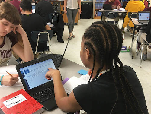 Student pointing at computer screen in classroom.