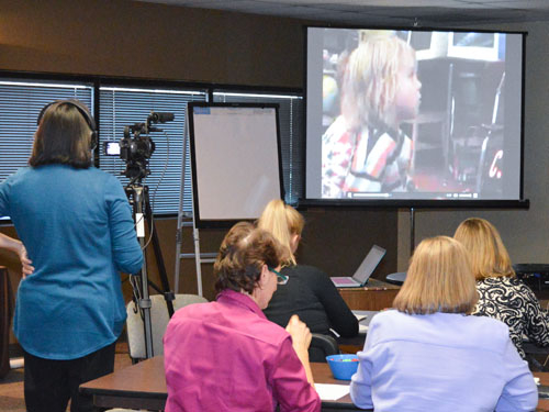 Women watching video of a child on a large screen.